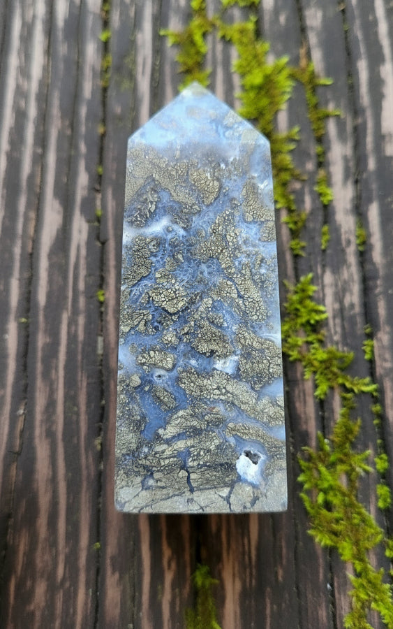 A small marcasite tower crystal with blue and gold coloring, held between fingers.