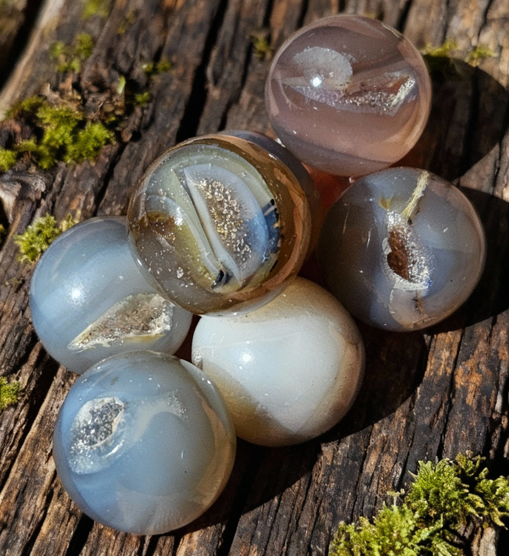 A collection of polished Druzy Agate mini spheres with varying shades of purple and brown, held in a person's hand.