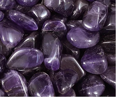 A close-up image of multiple polished Amethyst tumbles with a deep purple color.