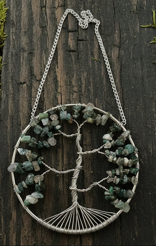 A silver-colored suncatcher featuring a Tree of Life design with moss agate crystals, displayed against a dark background.