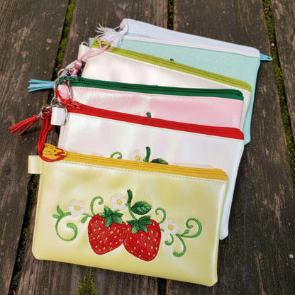 A collection of strawberry-themed zipper bags in various colors including pink, green, red, and yellow, each featuring embroidered strawberry designs and a keychain attachment.