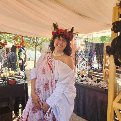 Person in a white dress with red patterns and floral headpiece standing outdoors.
