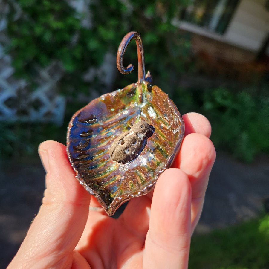 Hand holding a decorative copper leaf with a blurred outdoor background