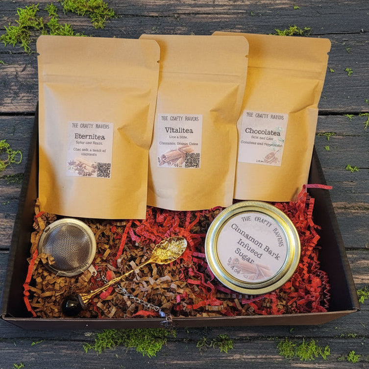 Gift set with tea bags, a strainer, and a tin labeled 'Cinnamon Bark Infused Sugar' on a red crinkled paper background.